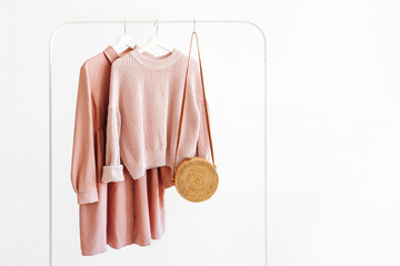 Feminine pale pink warm sweater and dress with bamboo bag on hanger on white background. Elegant   fashion outfit. Spring wardrobe. Minimal concept.