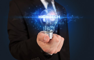 Businessman holding light bulb with HIGH-TECH inscription, innovative technology concept