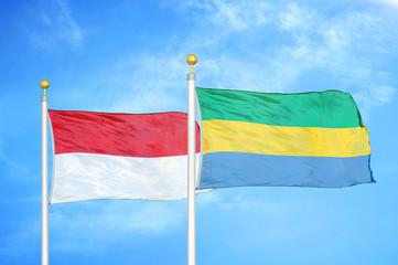 Indonesia and Gabon two flags on flagpoles and blue cloudy sky