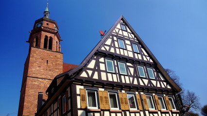 Turm der Stadtkirche von Weil der Stadt erhebt sich hinter einem Fachwerkhaus  vor blauem Himmel