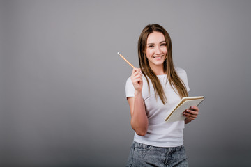 young woman with notebook and pencil writing isolated on grey background