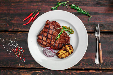 A large steak with spices and vegetables on the grill