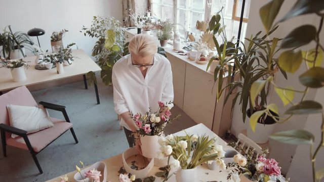 Tilt down high angle shot of professional female florist preparing floral composition in hatbox while working at table in large flower shop