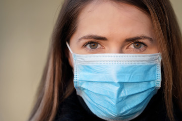 Young woman wearing disposable blue virus face mouth nose mask, closeup portrait. Coronavirus covid-19 outbreak prevention concept