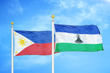 Philippines and Lesotho two flags on flagpoles and blue cloudy sky