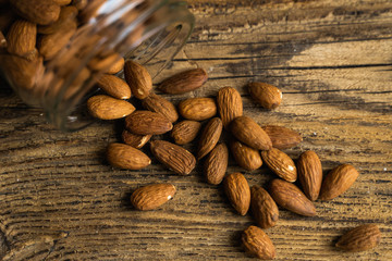 Almonds scattered on the wooden vintage table from a jar. Almond is a healthy vegetarian protein nutritious food. Almonds on rustic old wood.