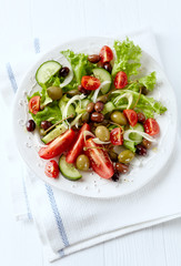 Healthy salad with various tomatoes, cucumber, olives and capers. White wooden background. Top view.	