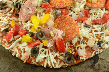 Frozen supreme pizza with peppers, olives, onions, pepperoni, canadian bacon and cheese on weathered cooking sheet