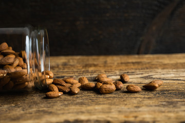 Almonds scattered on the wooden vintage table from a jar. Almond is a healthy vegetarian protein nutritious food. Almonds on rustic old wood.