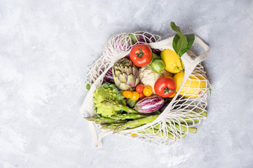 Different farm vegetables in a home string bag. Gray background. The concept of healthy eating.