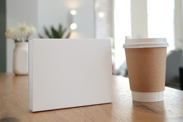 On the table is a mockup of a coffee cup and a white book. white box suitable for layout. Empty white background for design. White notebook. without text. Layout for overlaying your brand. Coffee 