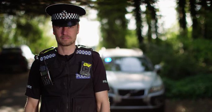 4K Portrait of UK traffic cop on patrol, car with lights flashing in background. Slow motion.