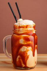 caramel milkshake with coffee on wooden table. Salted caramel ice cream sundae. Cold coffee drink frappe frappuccino , with whipped cream and caramel syrup