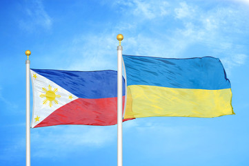 Philippines and Ukraine two flags on flagpoles and blue cloudy sky