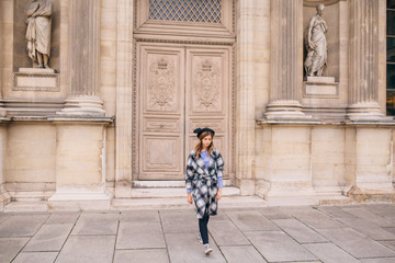 Fototapeta na wymiar A girl in a beautiful coat stands near the Louvre.
