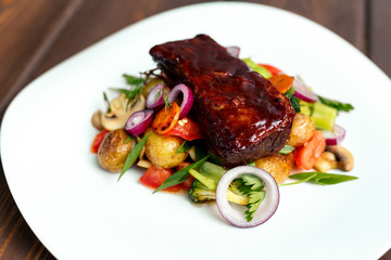 A calf steak with a young potato and juicy vegetables on a wooden background