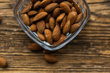 Almonds in a small plate with scattered nuts of almonds around a plate on a vintage wooden table as a background. Almond is a healthy vegetarian protein nutritious food. Natural nuts snacks.