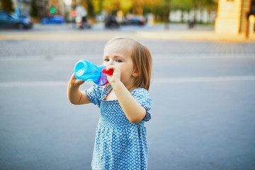 Adorable two year old girl drinking water on a street of Paris