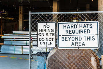 Signs at the entrance to a construction site stating that there is no hiring on site and hard hats are required beyond this area and cautioning people to not enter