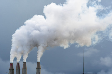Smoke and steam rising into the air from power plant stacks; dark clouds background; concept for...