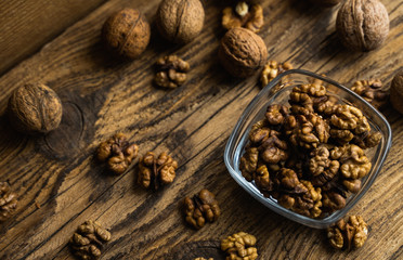 Walnut in a smale plate with scattered shelled nuts and whole nut which standing on a wooden vintage table. Walnuts is a healthy vegetarian protein nutritious food. Walnut on rustic old wood.