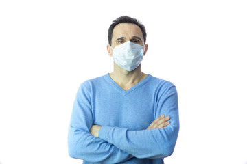 A middle-aged man with arms crossed on his chest is standing in the studio in a protective medical mask in order to be safe from viruses and infections.