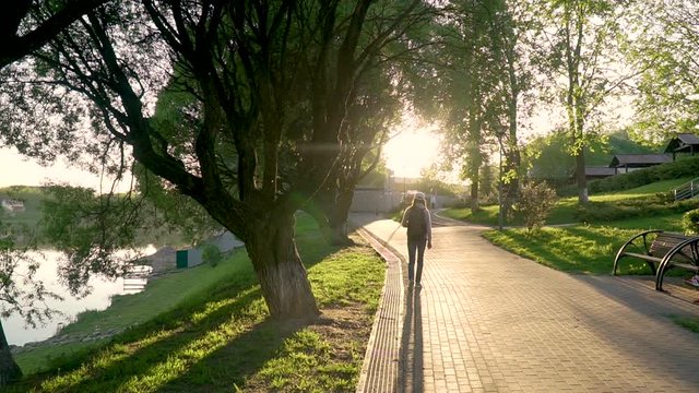 A girl walks along a path along the river bank in the rays of the setting sun