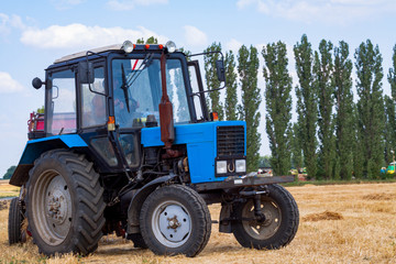 tractor makes big straw roll on yellow field at summer day
