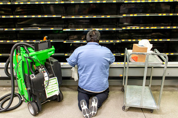 Worker cleaning empty shelves at a supermarket during the corona virus pandemic