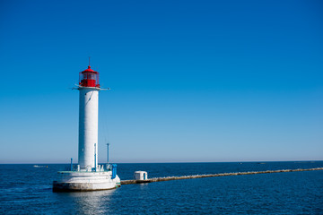 Fototapeta na wymiar A lighthouse stands in the sea on the water. The blue sea is far away, the shore is not visible. Bright blue sky, blue water