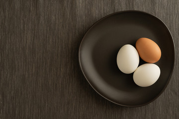One brown and two white eggs are on black plate and gray tablecloth