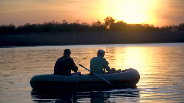 Two fishermen in the rays of the sunset catch fish from an inflatable boat