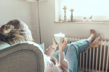 Junge Frau schaut aus dem Fenster und trinkt Tee