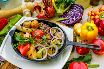 fried meat on the frying pan with vegetables and baked potatoes with vegetables