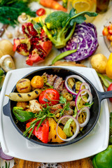 fried meat on the frying pan with vegetables and baked potatoes with vegetables
