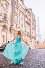 Fototapeta premium Beautiful young girl in a dress on the street with a view of the Eiffel tower
