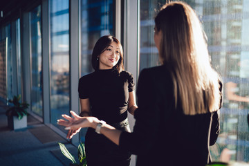 Young female managers in elegant wear discussing working issues gesturing and feeling confused during conversation, positive formally dressed woman showing don't know emotion talking to employee - obrazy, fototapety, plakaty