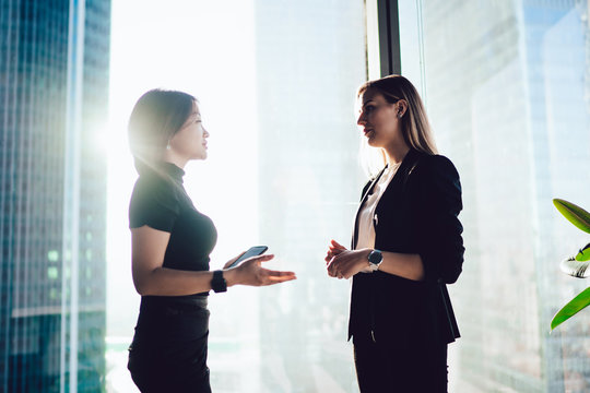 Diverse Female Managers In Elegant Wear Discussing Working Issues During Brainstorming Conversation In Enterprise, Multicultural Formally Dressed Women 30s Standing In Office Interior And Talking