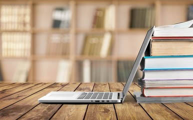 Stack of books with modern laptop on table