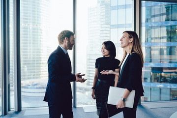 Cheerful  businessman in formal wear enjoying friendly conversation with female employees on work...