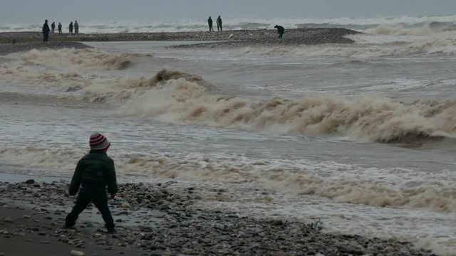 Cute children run away from sea waves on the beach in a stormy day