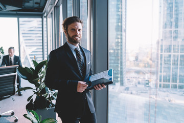 Cheerful half length portrait of confident male manager in formal suit standing with planner...