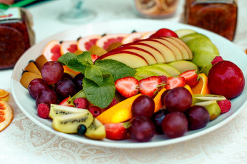 Naklejka na ściany i meble a plate of fruit assorted. Kiwi, grapefruit, oranges, apples, grapes and strawberries. On a white plate. Healthy food