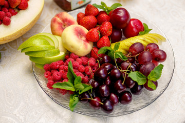 Fototapeta na wymiar berries and fruit in a transparent plate. Apples, pears, cherries, raspberries, plums, grapes.