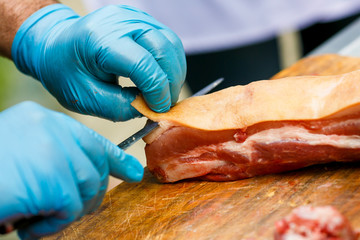 Close-up. A cook man in blue disposable gloves cuts a piece of red meat into pieces.