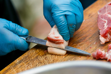 Close-up. A cook man in blue disposable gloves cuts a piece of red meat into pieces.