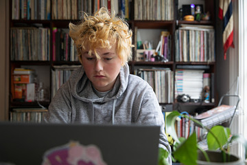 Blonde teenage male studying at home on his laptop
