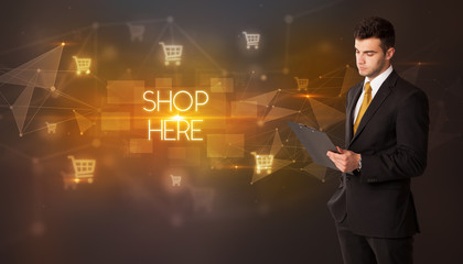 Businessman with shopping cart icons and SHOP HERE inscription, online shopping concept