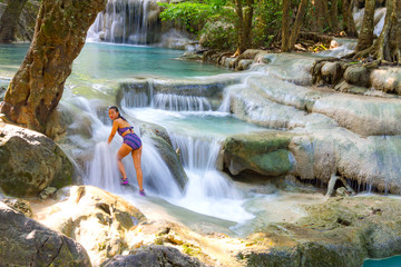 Travelerwoman in swimsuit enjoy on stone at Erawan Waterfall