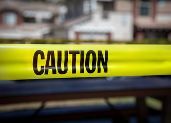 Yellow caution tape in english and spanish barring access to playgound equipment at a park. The access is denied due to the Coronavirus Pandemic